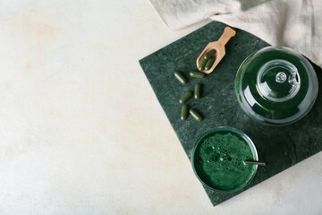 Glass and teapot of fresh spirulina drink on beige grunge background