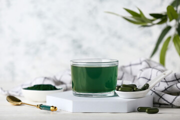 Glass of fresh spirulina drink and pills on white wooden table, closeup