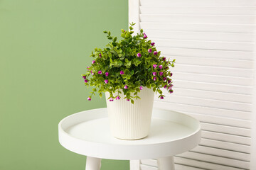 Artificial flowers on table and folding screen near green wall