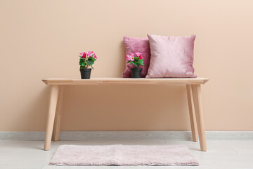 Naklejka premium Pink artificial flowers with pillows on table near beige wall in room