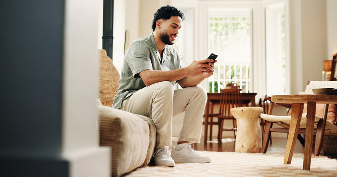 Man, typing and smile with phone on couch for social media notification, online dating and virtual chat. Happy, person and scroll in home with tech for text message, browsing internet and mobile app. - Powered by Adobe
