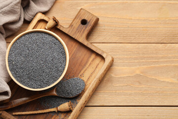 Bowl and spoon with poppy seeds on wooden background, closeup