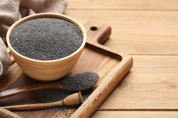 Bowl and spoon with poppy seeds on wooden background, closeup