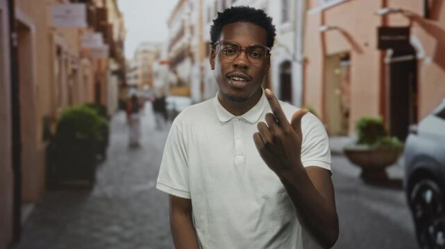 Man wearing white polo shirt beckons finger on urban street amid buildings and blurred pedestrians; friendly invitation.
