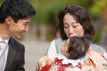 A man and a woman are holding a baby. The man is smiling and the woman is kissing the baby. Scene is happy and loving