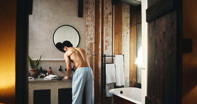 Back, basin and doorway with shirtless man in bathroom of hotel room for hygiene or morning routine. Entrance, start and wake up with person at sink for accommodation, break or hospitality as guest - Powered by Adobe