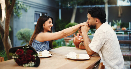 Happy, couple and holding hands in restaurant, kiss and bonding on anniversary and date with partner. Outdoor, man and affection for woman on valentines day, bouquet or roses for celebration and love