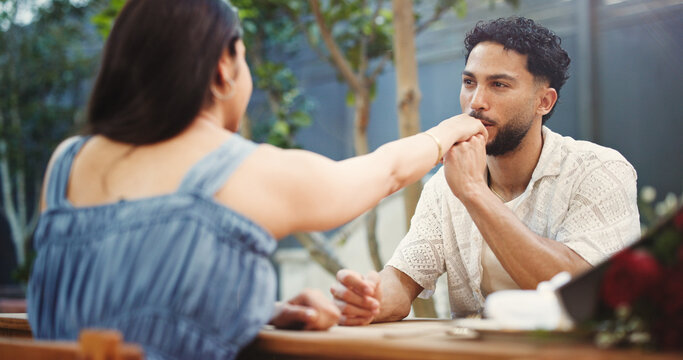 Couple, holding hands and kiss on date at restaurant with bouquet, discussion and relationship milestone. Happy man, woman and connection with bonding, trust and flowers for anniversary at diner