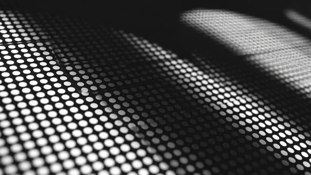 Abstract black and white macro shot of a perforated metal surface with dramatic light and shadow patterns creating a geometric texture background
