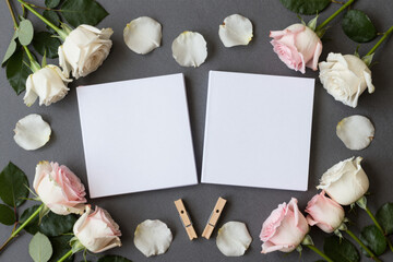 Elegant flat lay composition featuring delicate pink and white roses framing two blank white cards, perfect as a romantic or wedding background