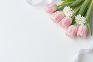 Fresh pink tulips and delicate white filler flowers with a flowing white ribbon arranged on a clean white background, perfect for spring or romantic designs