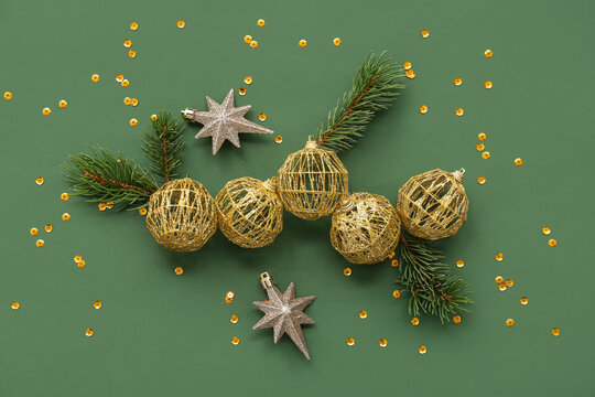 Composition with golden Christmas balls, confetti and fir tree branches on green background