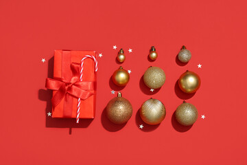 Composition with golden Christmas balls, gift box and confetti on red background