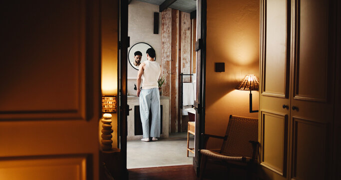 Back, basin and doorway with man in bathroom of hotel room for hygiene or morning routine. Entrance, start and wake up with guest person at sink of lodge for accommodation, break or hospitality