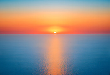 Obraz premium Sun dropping into ocean at horizon line during sunset