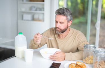Latin Man eat breakfast in the kitchen on a morning. Guy eat vegetables for a healthy meal in his kitchen in the morning. Cozy kitchen. Morning breakfast in the white kitchen.