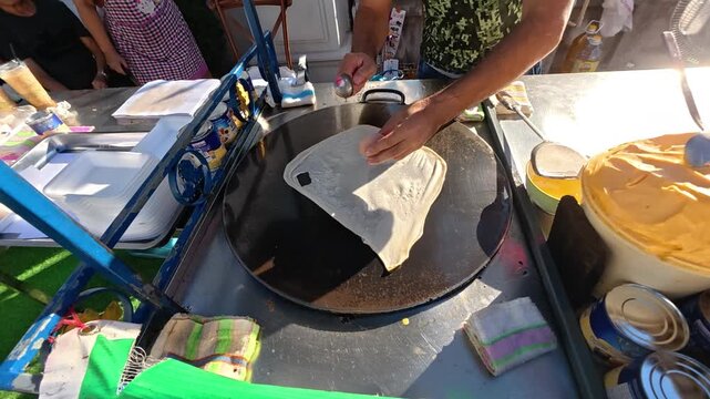 Roti Preparation: A skilled cook meticulously prepares a roti on a hot griddle, capturing the art of traditional culinary techniques in a bustling outdoor setting.