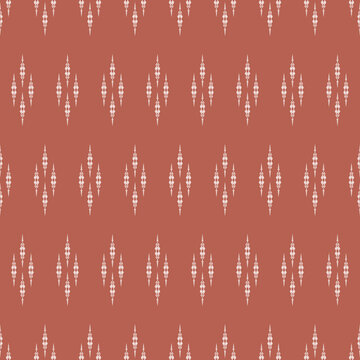Seamless traditional Ikat pattern. Rustic white tribal diamond motif on terracotta background. Earthy bohemian textile and wallpaper texture.
