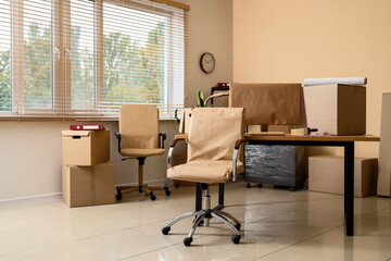 Desk with chairs and cardboard boxes in office on moving day