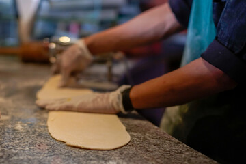 Close-up of a chef’s gloved hands shaping dough on a kitchen countertop. Warm lighting and a working culinary environment emphasize themes of food preparation