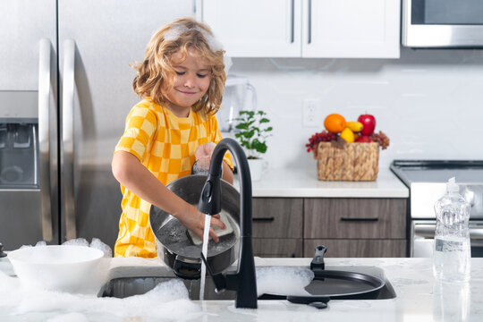 Child washing dishes with foam. Kid play with soap bubbles at kitchen. Cute child cleaning dishes with foam. Kid washing dishes. Playful boy with soap bubbles. Child fun with dish soap at sink.