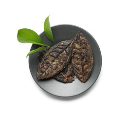 Plate with dry pressed puer tea and fresh leaves on white background