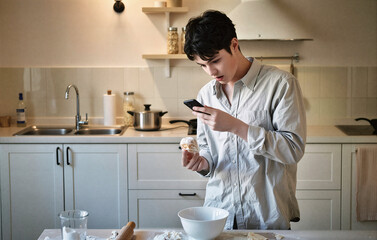 Young man taking photo of pastry with smartphone in kitchen