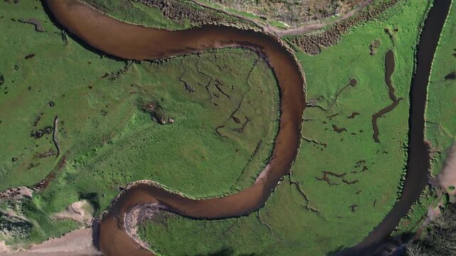 Top down drone ascent revealing the winding Pennard Pill river through lush green fields near Three Cliffs Bay in Wales