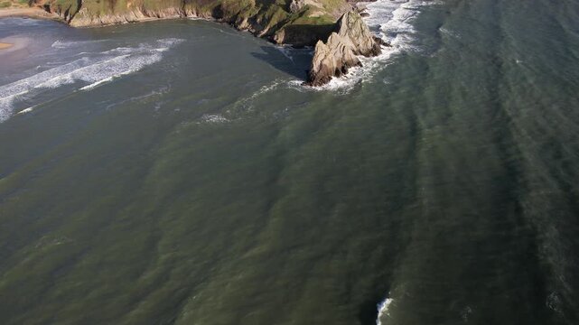 Drone approaching jagged cliffs and green coastline revealing Pobbles Bay and the surrounding headlands in South Wales