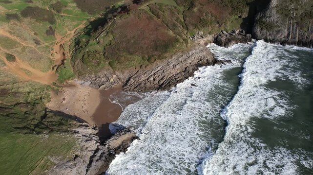 Drone circling above Pobbles Bay showing powerful dramatic rocks and rolling green cliffs on the Welsh coast