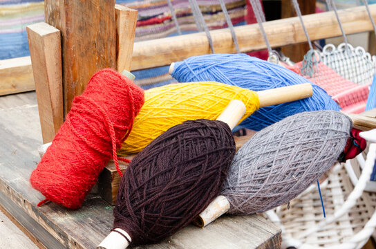 A close-up shot of several spools of colorful yarn, including red, yellow, black, blue, and gray, resting on a rustic wooden surface.
