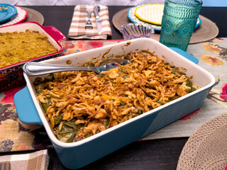Green bean casserole topped with crispy fried onions in a blue baking dish on a festive holiday table. Colorful plates and decor make it perfect for Thanksgiving and family meal themes.