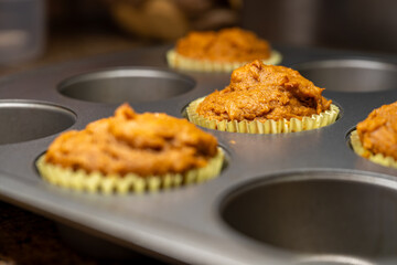 Fresh pumpkin muffin batter baking in a metal muffin pan, captured with shallow depth of field. Warm, cozy scene ideal for fall recipes, Thanksgiving content, food blogs, and seasonal baking themes.