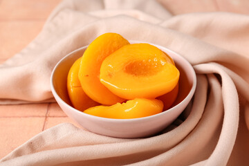 Bowl with sweet canned peaches on beige tile background, closeup