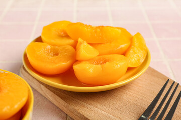 Plate with sweet canned peaches on pink tile background, closeup