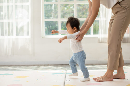 Asian Baby learning to walk with gentle family guidance in bright living room creating joyful early milestone moment