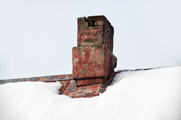 Old brick chimney on a snowy roof against a bright, overcast sky