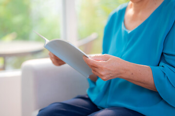 Close up asian senior woman reading book sitting on sofa with relax in living room at home, elderly woman reading literature on couch with cozy, hobby and recreation in weekend, lifestyles concept.