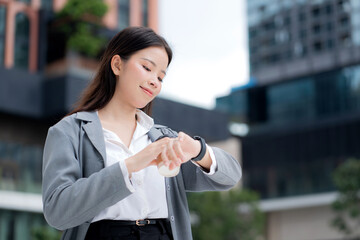 Young asian businesswoman checking time on smartwatch while waiting on busy city street, professional business woman with confident smile managing schedule and appointment in business district.
