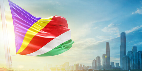 Seychelles flag wavering in beautiful clouds with building skyline. The flag with drone shot in beautiful sky. Seychelles national flag for independence day.