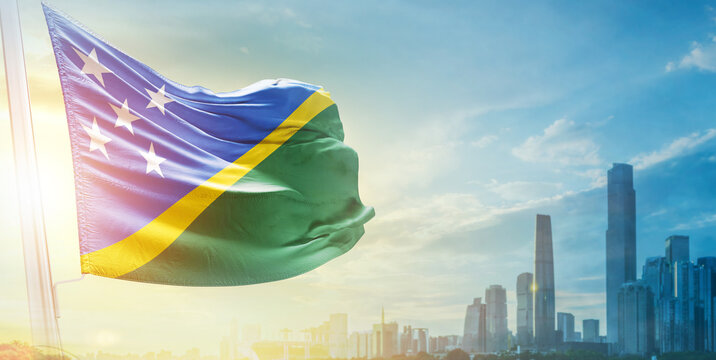 Solomon Islands flag wavering in beautiful clouds with building skyline. The flag with drone shot in beautiful sky. Solomon Islands national flag for independence day. - Powered by Adobe