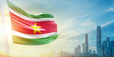 Suriname flag wavering in beautiful clouds with building skyline. The flag with drone shot in...