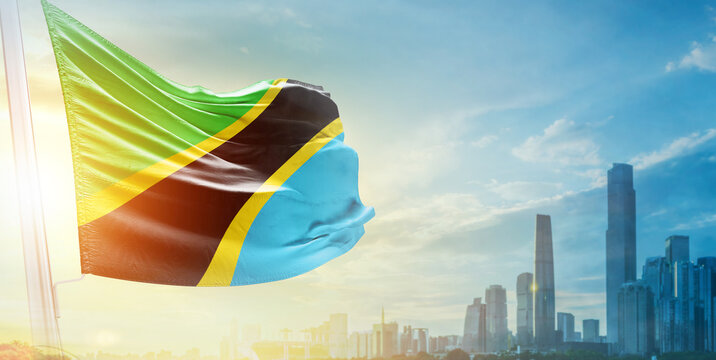 Tanzania flag wavering in beautiful clouds with building skyline. The flag with drone shot in beautiful sky. Tanzania national flag for independence day. - Powered by Adobe
