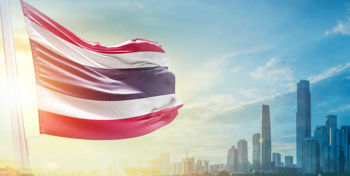 Thailand flag wavering in beautiful clouds with building skyline. The flag with drone shot in beautiful sky. Thailand national flag for independence day. - Powered by Adobe