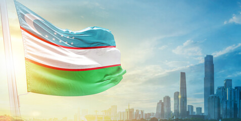 Uzbekistan flag wavering in beautiful clouds with building skyline. The flag with drone shot in beautiful sky. Uzbekistan national flag for independence day.