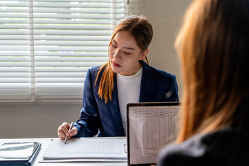 Businesswoman sitting at desk on couch in workplace or at home working on laptop and analyzing data on charts and graphs and writing on papers to make business plan and strategies for company, 