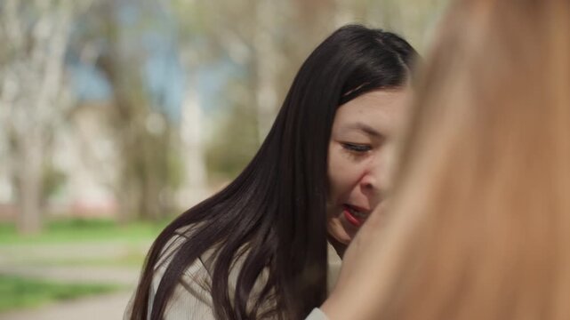 asian woman sneezes into tissue outdoors, red eyes and runny nose from pollen, scarf and jacket visible, birch trees and park path in background, vulnerable emotional moment and physical discomfort