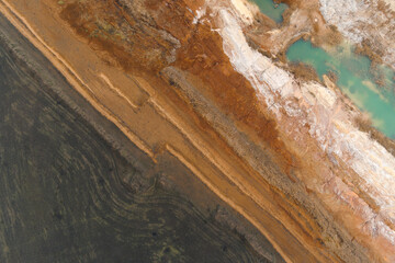 Obraz premium Top-down abstract aerial view of a sharp diagonal contrast between dark tilled soil and multicolored geological quarry layers.