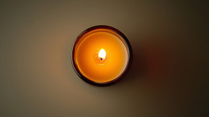 A warm, glowing tealight candle burns from a top-down perspective, its small flame gently flickering above a pool of melted wax. The soft, circular glow radiates outward, creating a cozy and intimate