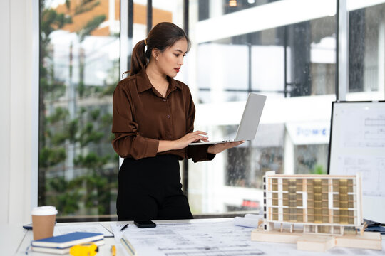 Young female engineer designer or contractor working on drawing plans analyzing structure on laptop computor at construction site office. copy space.